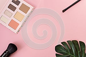 Professional makeup tools palette of multicolor cosmetic make up set with brushes and a monstera leaf on pink background. Beauty