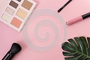 Professional makeup tools palette of multicolor cosmetic make up set with brushes and a monstera leaf on pink background. Beauty