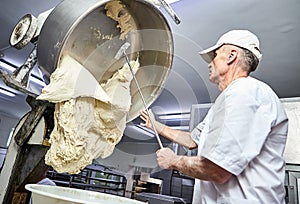 Professional male Baker mix dough with professional kneader machine at the manufacturing. Equipment for making flour products