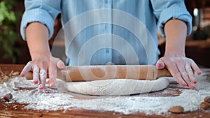 Professional male baker rolling out dough for bread or pasta on table, closeup view of hands, bakery