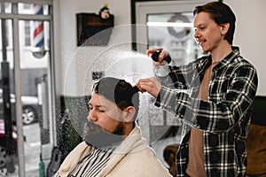 professional male barber splashes water from the spray bottle at the head hair of his client