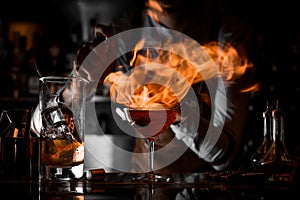 Professional male bartender putting fire from the lighter on the cocktail glass