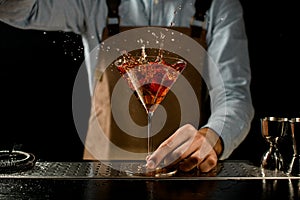 Professional male bartender throwing a red rose bud to a martini glass with a golden cocktail