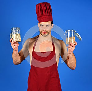 Professional male cook in chef hat and apron holds glass jars with groats and cereals. Breakfast and healthy diet. Grit