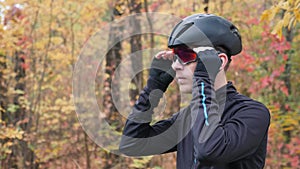 Professional male cyclist in black sports apparel and helmet preparing for training in autumn park and puts on glasses. Cycling tr