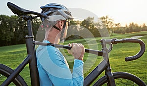 Professional male cyclist wearing sportswear and protective helmet looking aside while carrying his bike after training
