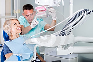 professional male dentist explaining future treatment to female patient on dental model