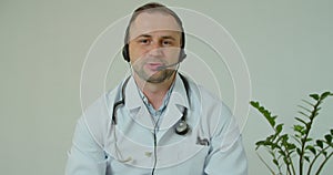 Professional male doctor in white medical coat and headset making conference call on laptop computer, consulting
