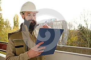 Professional male foreman in helmet during inspection in construction site, bearded man in uniform, contractor, architect on