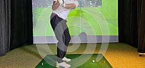 Professional male golfer holding club playing golf indoors on golf simulator