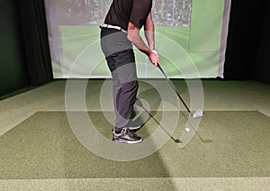 Professional male golfer holding club playing golf indoors on golf simulator