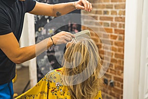 Professional male hairdresser spraying and styling with comb his female client& x27;s blonde hair in the professional