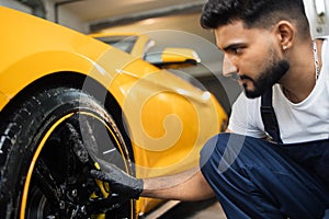 Professional male in overalls and protective gloves, cleaning alloy wheels rims of luxury car