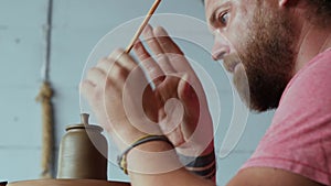 Professional male potter forms a handle to the lid of a clay teapot on a potter`s wheel. art craft. craft work concept