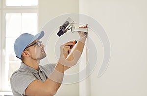 Professional male surveillance camera installer mounts it on wall inside new home or office.