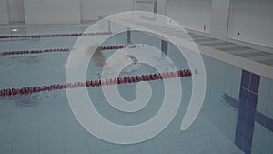 Professional male swimmer in indoor pool swimming across track. Healthy lifestyle. Sports and recreation.