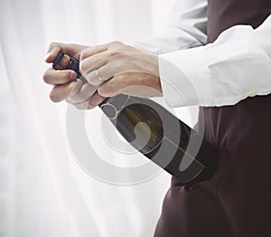 Professional male waiter in uniform opening bottle of champagne