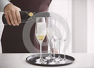 Professional male waiter in uniform pouring champagne into a flu