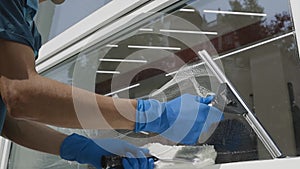 Professional male worker in overalls is engaged in cleaning and washing windows with special foam and tools in slow