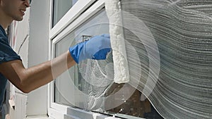 Professional male worker in overalls is engaged in cleaning and washing windows with special foam and tools in slow