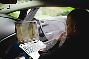 Professional man with a laptop in car tunes tuning control system, updating software, gaining access through to computer