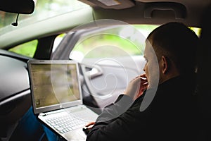 Professional man with a laptop in car tunes tuning control system, updating software, gaining access through to computer