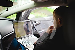 Professional man with a laptop in car tunes tuning control system, updating software, gaining access through to computer