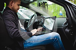 Professional man with a laptop in car tunes tuning control system, updating software, gaining access through to computer