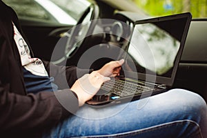 Professional man with a laptop in car tunes tuning control system, updating software, gaining access through to computer