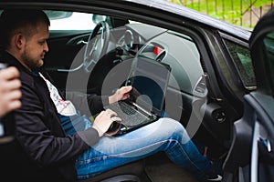 Professional man with a laptop in car tunes tuning control system, updating software, gaining access through to computer