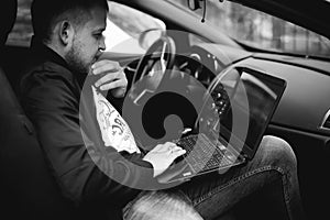 Professional man with a laptop in car tunes tuning control system, updating software, gaining access through to computer