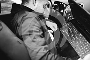 Professional man with a laptop in car tunes tuning control system, updating software, gaining access through to computer