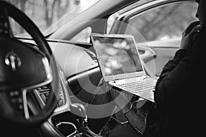 Professional man with a laptop in car tunes tuning control system, updating software, gaining access through to computer