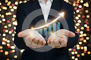 Professional man in suit with glowing upward graph in hands, surrounded by festive lights, symbolizing growth