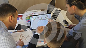 Professional managers comparing sales result graphs on papers with chart on computer screen at office. Group of young