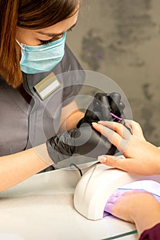 Professional manicure. A manicurist is painting the female nails of a client with purple nail polish in a beauty salon