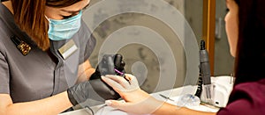 Professional manicure. A manicurist is painting the female nails of a client with purple nail polish in a beauty salon