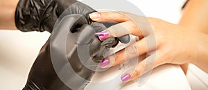 Professional manicure. A manicurist is painting the female nails of a client with purple nail polish in a beauty salon