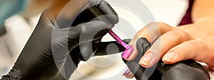 Professional manicure. A manicurist is painting the female nails of a client with purple nail polish in a beauty salon