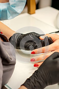 Professional manicure. A manicurist is painting the female nails of a client with red nail polish in a beauty salon