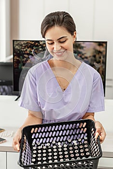 Professional manicure master in purple uniform holds nail varnish bottles. Manicurist and pedicurist waiting for clients