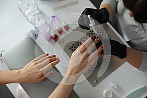 Professional manicurist pouring oil on client`s nails in salon, top view