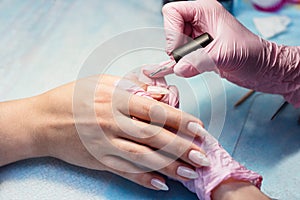 A professional manicurist puts color gel nail Polish brush on the finger of the client after applying the shellac.