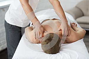 Professional massage therapist is treating a male patient in apartment.