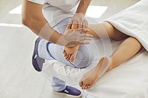 Professional masseur doing foot massage for young woman in modern health clinic