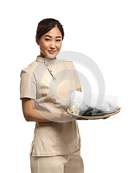 Professional masseuse in spa uniform holding tray with towel and rocks photo