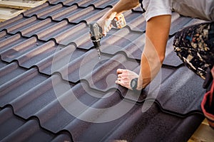 Professional master (roofer) with electric screwdriver covers repairs the roof