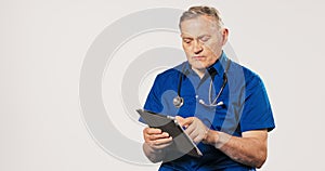 Professional, mature doctor dressed in blue uniform, gown and stethoscope around his neck, clicks away