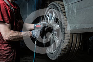 A professional mechanic in the service center checks the suspension of the dirty car and Performs seasonal wheel replacement..