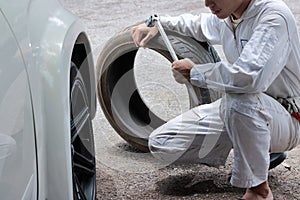 Professional mechanic in uniform holding wrench and tire at the repair garage background.